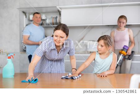 Cheerful woman wiping table in kitchen with preteen daughter 130542861