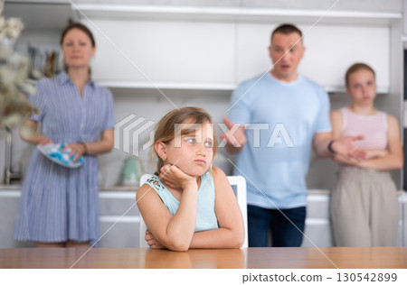 At home kitchen parents scold sitting child for bad behavior, mother clean dish in background 130542899