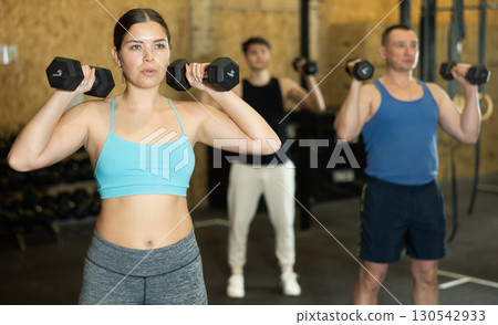 Concentrated young girl pumping up deltoid muscles with dumbbells 130542933