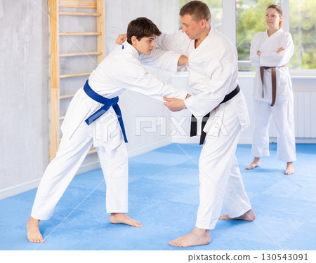 Male athletes in pair conduct training battle in oriental fighting technique under guidance of coach 130543091