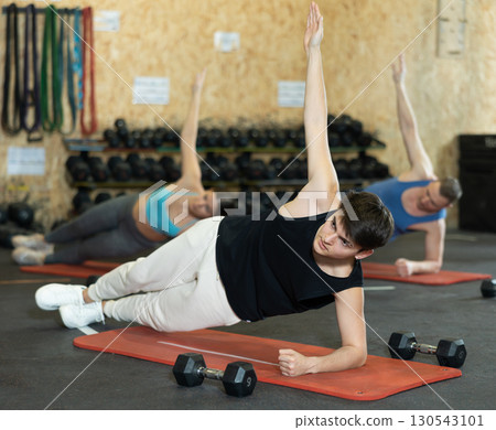 Guy holding side plank pose during group training in gym Guy holding side plank pose during group training in gym 130543101