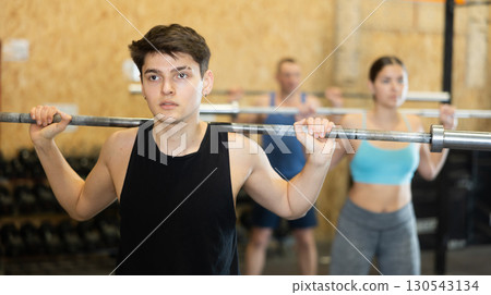 Young male bodybuilder performing strength and endurance exercises during group barbell lifting in CrossFit class 130543134