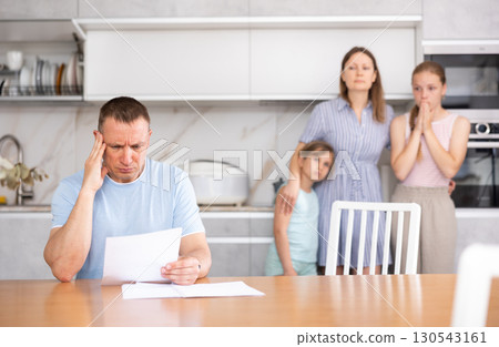 Disgruntled father carefully reads documents. The whole family stands in fear in background 130543161