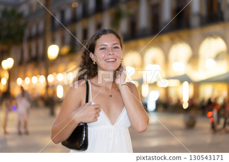 In evening, young smiling girl walks along city street Placa Real 130543171