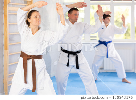Woman and man in kimono standing in fight stance during group karate training in gym 130543176