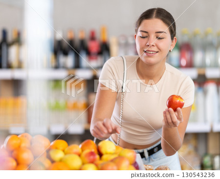 Near counter, young woman client takes out apples from pile of fruits, chooses ripe fruits 130543236