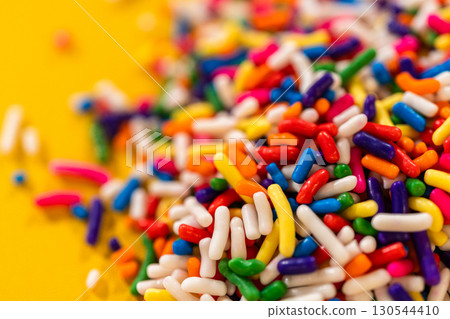 A close-up view of vibrant candy sprinkles scattered on a bright yellow surface. Perfect for backgrounds, party invitations, birthday themes, or dessert advertisements. 130544410
