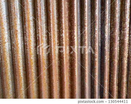 Detailed view of a weathered corrugated metal siding with visible rust texture and natural patina. The metal panels offer an industrial, aged appearance with vertical lines. 130544411