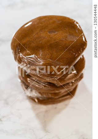 Stacked portions of Spiced Gingerbread Cookie Dough Perfect for Baking wrapped in plastic wrap. The dough is divided for easy handling and chilled, ready for rolling and shaping into cookies. 130544448
