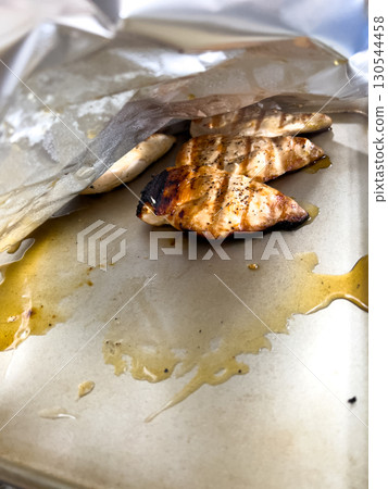 Grilled chicken breasts rest on a foil-lined baking sheet, still showing char marks and slight juices around the edges. The lighting is natural and the scene captures the texture of cooked meat. Grilled chicken breasts rest on a foil-lined baking sheet, still showing char marks and slight juices around the edges. The lighting is natural and the scene captures the texture of cooked meat. 130544458
