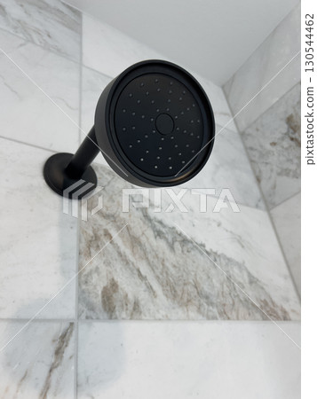 View of a matte black shower head mounted on a veined marble-tiled wall. The shower head contrasts beautifully with the clean tile design. Perfect for home improvement content or interior design 130544462