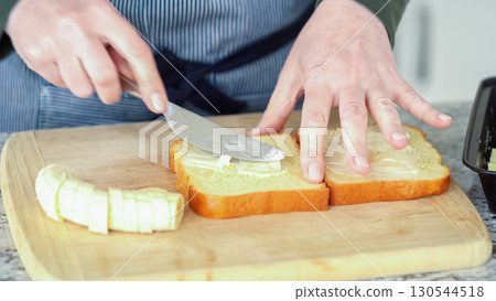 In a modern white kitchen, buttered banana and brioche bread are being prepared for making a delicious grilled peanut butter banana sandwich. 130544518