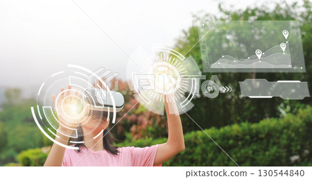Girl using virtual reality headset with futuristic digital interface, hologram data visualization, AR VR technology, innovation, learning, education and future concept outdoors. Girl using virtual reality headset with futuristic digital interface, hologram data visualization, AR VR technology, innovation, learning, education and future concept outdoors. 130544840