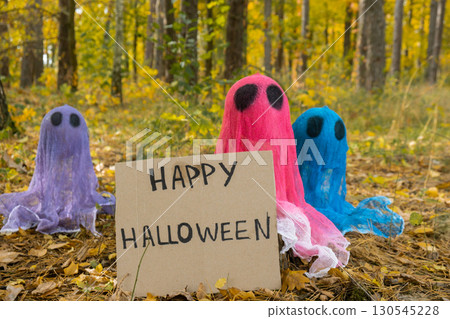 Halloween holiday concept. Handmade colorful ghosts with cardboard HAPPY HALLOWEEN message made from bandages and glue in autumn forest background. Children's art project. DIY Halloween holiday concept. Handmade colorful ghosts with cardboard HAPPY HALLOWEEN message made from bandages and glue in autumn forest background. Children's art project. DIY 130545228