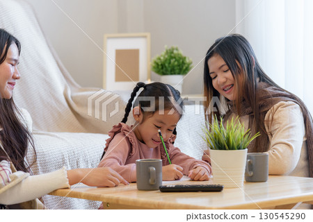 During a warm winter day a child enjoys drawing while sitting with two adults at a table with beverages and a plant, showcasing a moment of creativity and connection indoors. During a warm winter day a child enjoys drawing while sitting with two adults at a table with beverages and a plant, showcasing a moment of creativity and connection indoors. 130545290