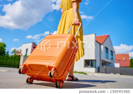 Woman walking with suitcase in suburban neighborhood 130545360