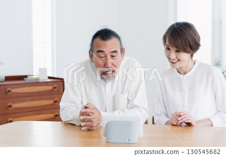 Senior couple talking to a smart speaker in the living room Senior couple talking to a smart speaker in the living room 130545682