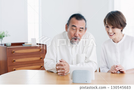 Senior couple talking to a smart speaker in the living room 130545683