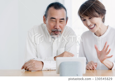 Senior couple talking to a smart speaker in the living room Senior couple talking to a smart speaker in the living room 130545829