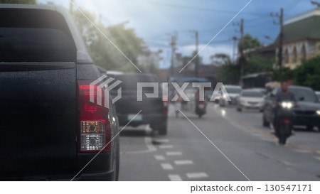Rear side of pickup car black color. Car parking side of asphalt road. Other cars and motorcycle driving in the city at day time. 130547171