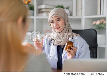 Knowledgeable female doctor in hijab discussing medication options with a patient in her office. Knowledgeable female doctor in hijab discussing medication options with a patient in her office. 130547667