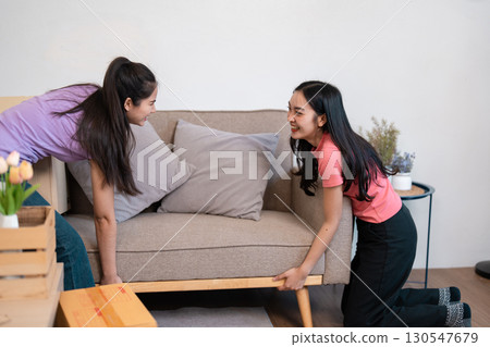 Diverse female couple smiling while moving a sofa into their new living room. Diverse female couple smiling while moving a sofa into their new living room. 130547679