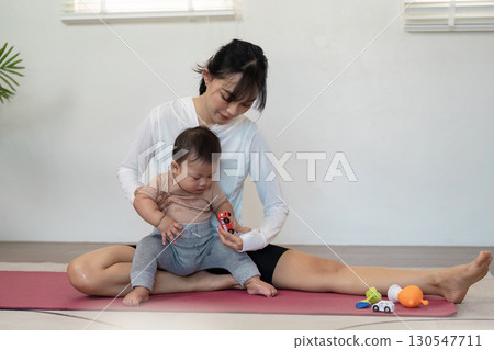 Mother engaging in playful interaction with her baby during a yoga session at home, promoting family bonding and wellness. 130547711