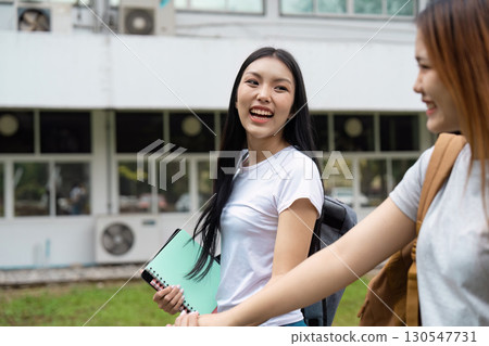 Two vibrant students sharing a joyful moment on campus, one holding a notebook and the other smiling brightly Two vibrant students sharing a joyful moment on campus, one holding a notebook and the other smiling brightly 130547731