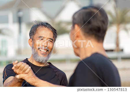 Cheerful senior Asian men sharing a handshake and laughter on a sports field, celebrating wellness and friendship. Cheerful senior Asian men sharing a handshake and laughter on a sports field, celebrating wellness and friendship. 130547813