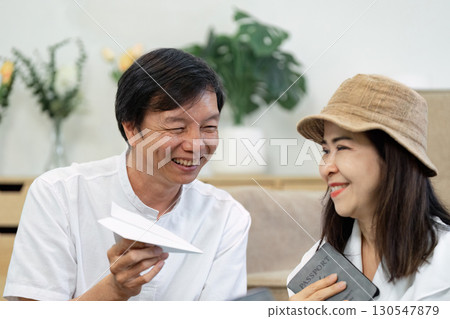 Senior couple excitedly discussing travel plans while holding a passport and paper airplane. 130547879