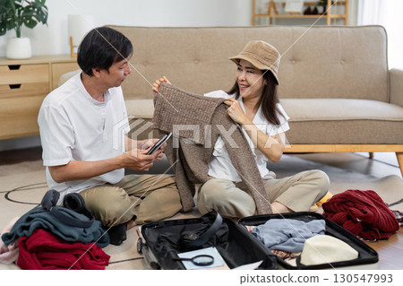 Senior couple happily packing travel clothes and planning their trip in a cozy living room. 130547993