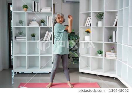 Senior woman performing stretching exercises at home, focusing on wellness and mobility. 130548002