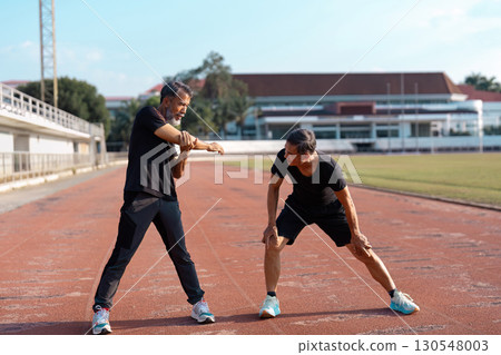 Active older Asian men stretching together on a track, promoting wellness and fitness. 130548003