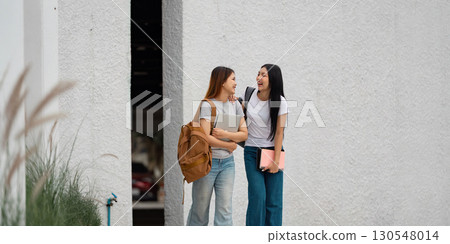 Diverse university students laughing and chatting together outdoors near a wall. 130548014