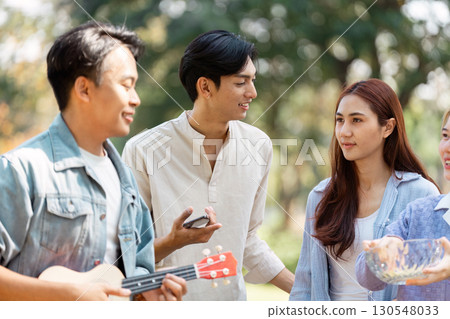 Friends having a fun conversation while enjoying music at a picnic in the park. 130548033