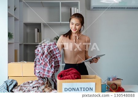 Diverse young woman organizing clothing donations in a community space, promoting charity and social responsibility. Diverse young woman organizing clothing donations in a community space, promoting charity and social responsibility. 130548088