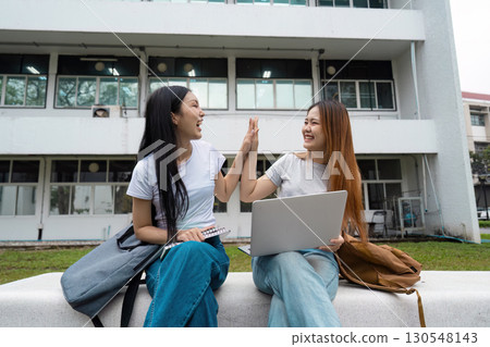 Diverse female students celebrating success with a high-five at university. 130548143
