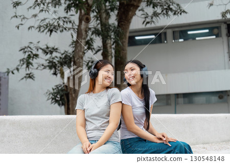 Diverse female students enjoying music together with headphones on campus. Diverse female students enjoying music together with headphones on campus. 130548148