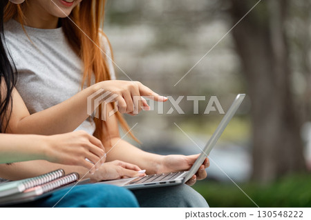 Students collaborating and engaging with a laptop in a vibrant outdoor setting 130548222