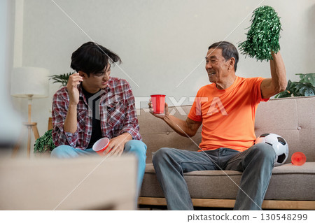 Excited older man celebrating soccer while young family member reacts at home Excited older man celebrating soccer while young family member reacts at home 130548299