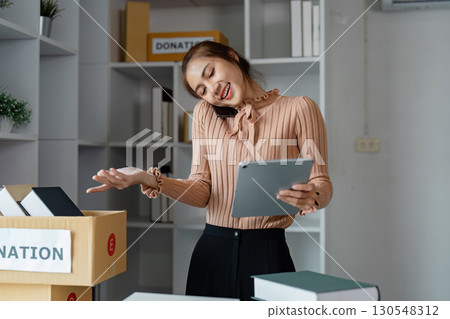Woman managing online donations with a tablet and phone at a charity organization. Woman managing online donations with a tablet and phone at a charity organization. 130548312