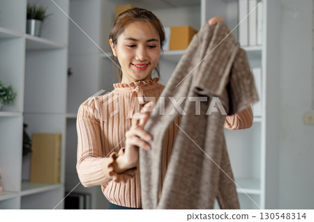 Smiling young woman examining a sweater while organizing clothing donations in a community space, promoting charity and joy. 130548314