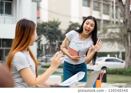 Diverse female student greeting friend while holding notebooks outdoors. 130548348