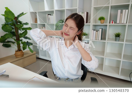 Neck Tension. Young woman feeling discomfort while sitting at her desk in a modern office. 130548370