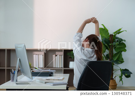 Remote Work. Young woman stretching her arms at her desk to alleviate tension. 130548371