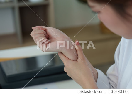 Mental Health Awareness. Young woman checking pulse at desk, reflecting on stress and wellness. 130548384