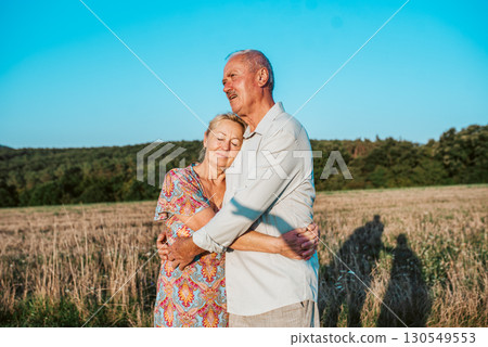 Happy senior couple embracing in meadow at sunset. 130549553
