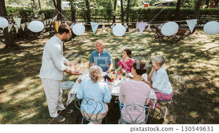 Areal view of grandparents, parents and kids dining together outside. Areal view of grandparents, parents and kids dining together outside. 130549631