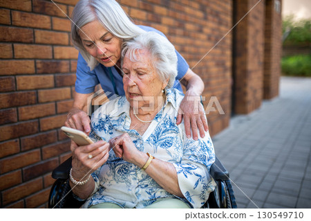 Senior patient in wheelchair showing picture in smartphone to caregiver. 130549710