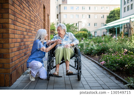 Senior patient in wheelchair talking with her caregiver. Senior patient in wheelchair talking with her caregiver. 130549715
